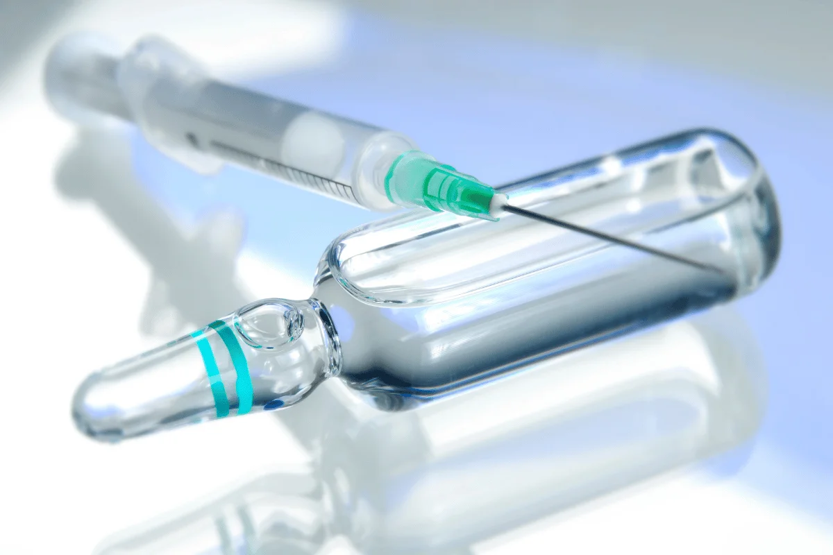 Close-up of a syringe and a glass ampoule on a reflective surface.