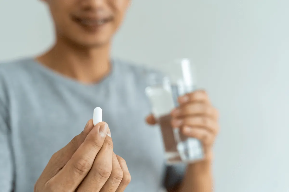 Person holding a white pill and a glass of water, preparing to take medication.