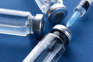 Sterile glass vials with silver caps next to a syringe.