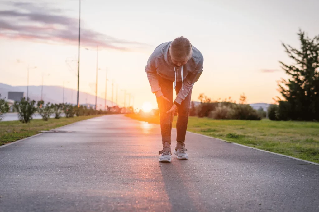 Jogger holding their knee while resting on a path during sunset.