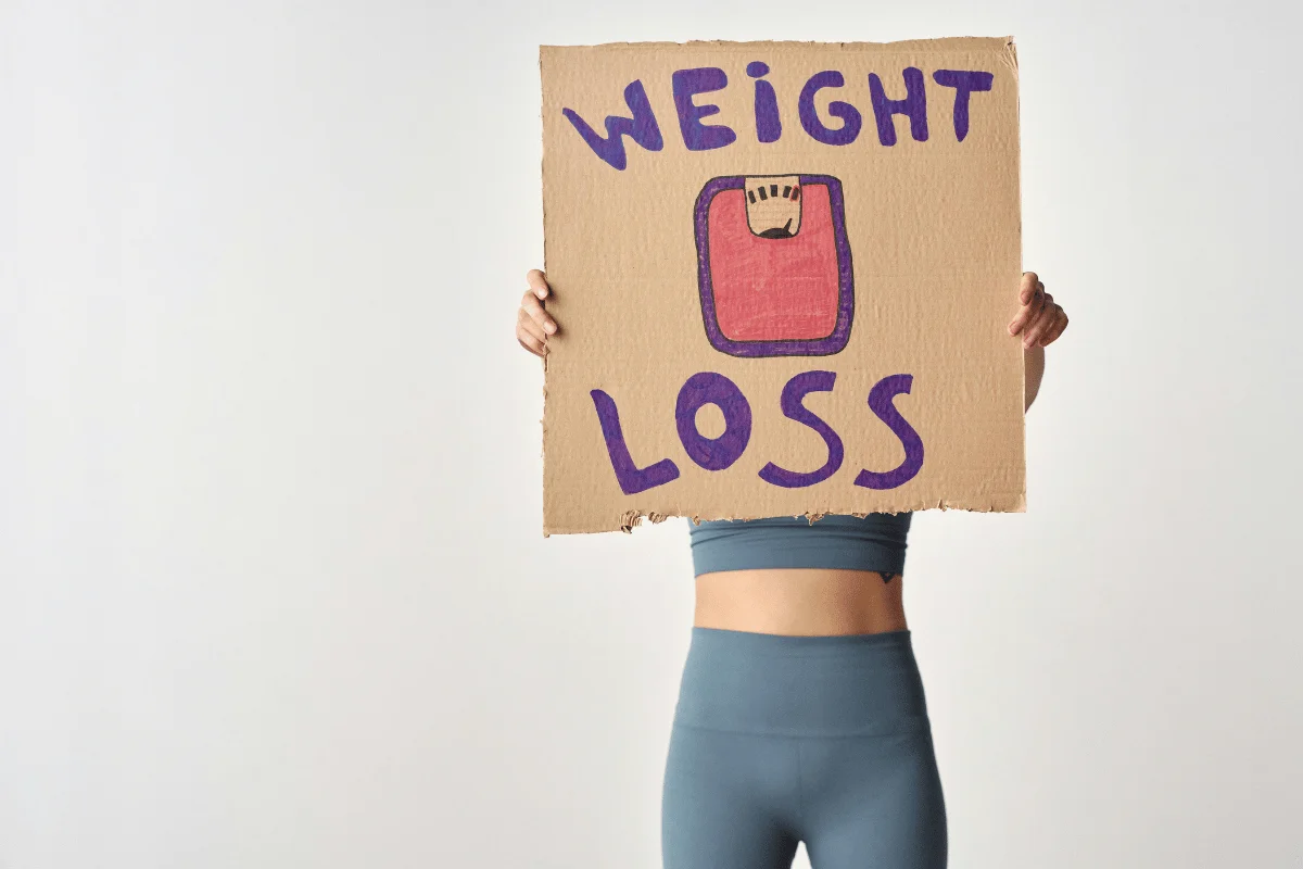 Person holding a cardboard sign with 'Weight Loss' written and an illustration of a scale.