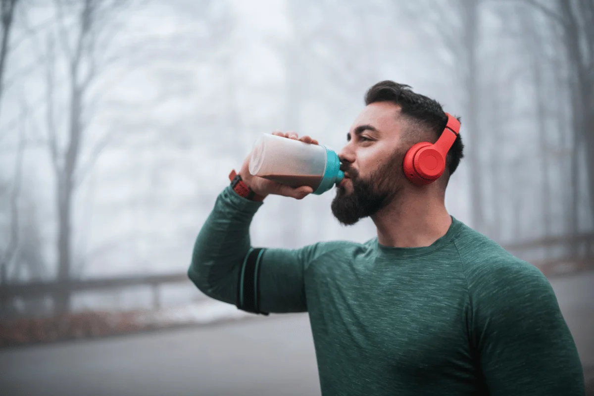 Man wearing red headphones drinking a protein shake during an outdoor workout.