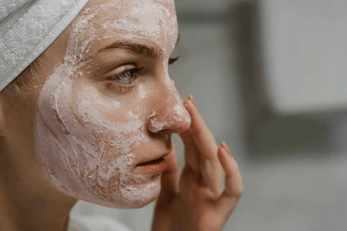 Close-up of a woman applying a creamy face mask while wearing a towel wrap.