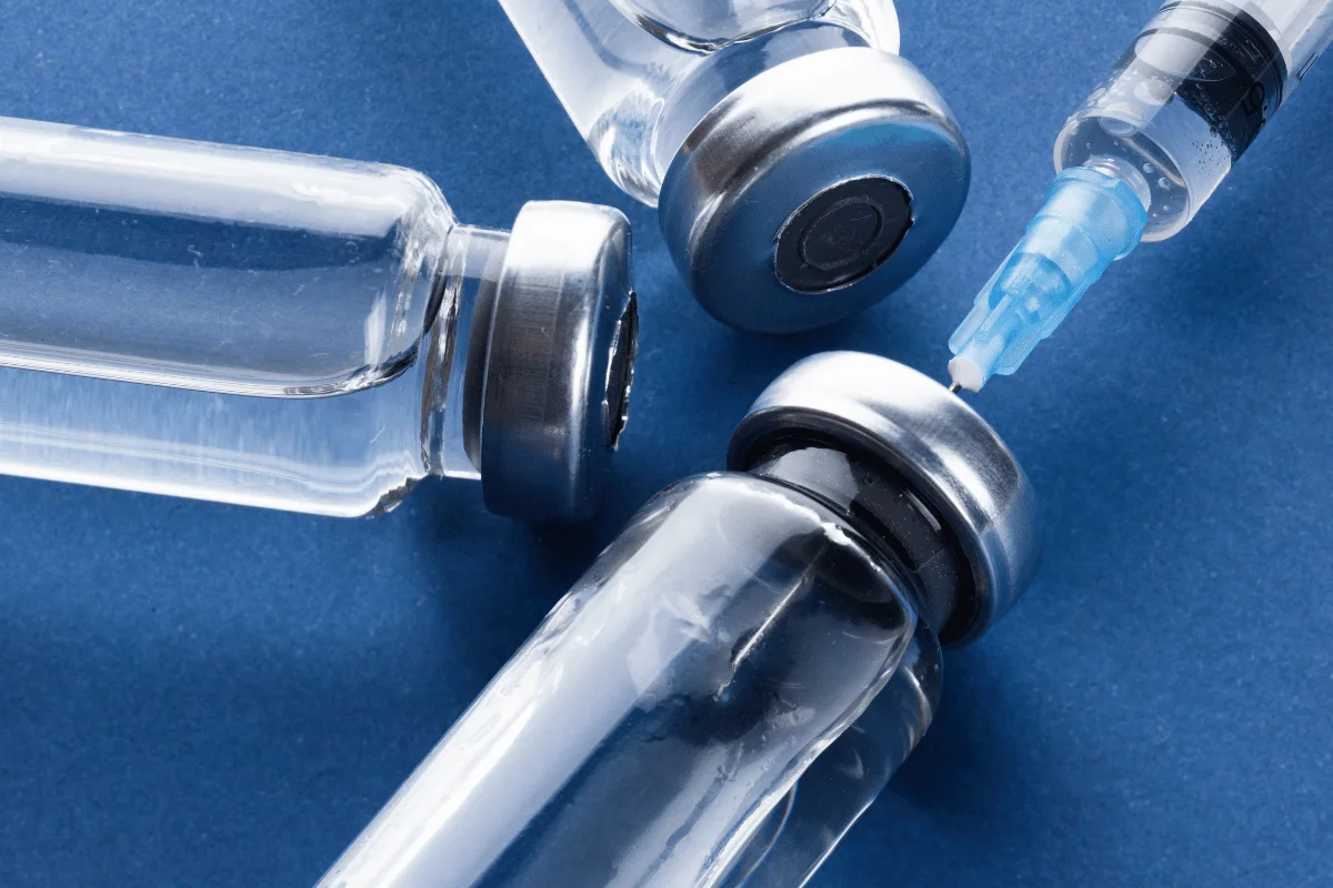 Close-up of medical vials and syringe on a blue background.