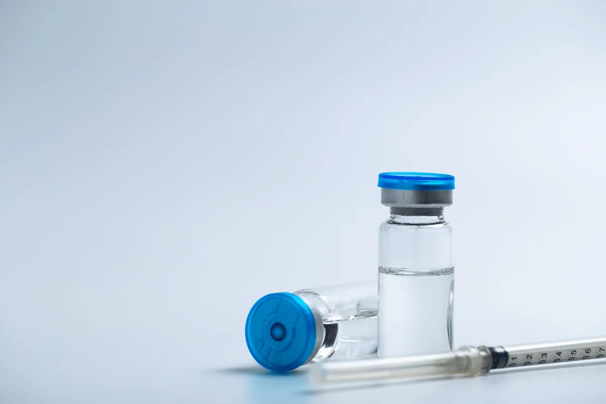 Glass vials with blue caps and a medical syringe on a light background.