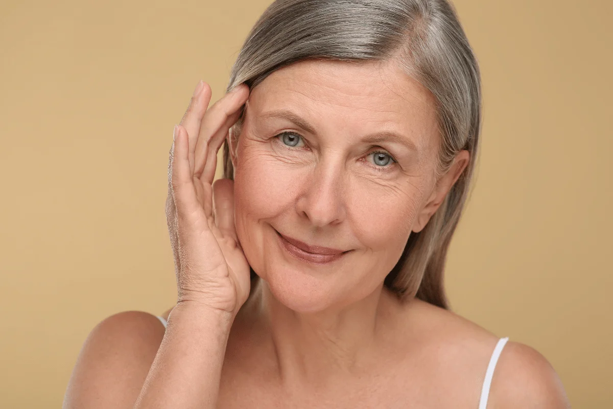 Portrait of an older woman with gray hair smiling gently and touching her face.