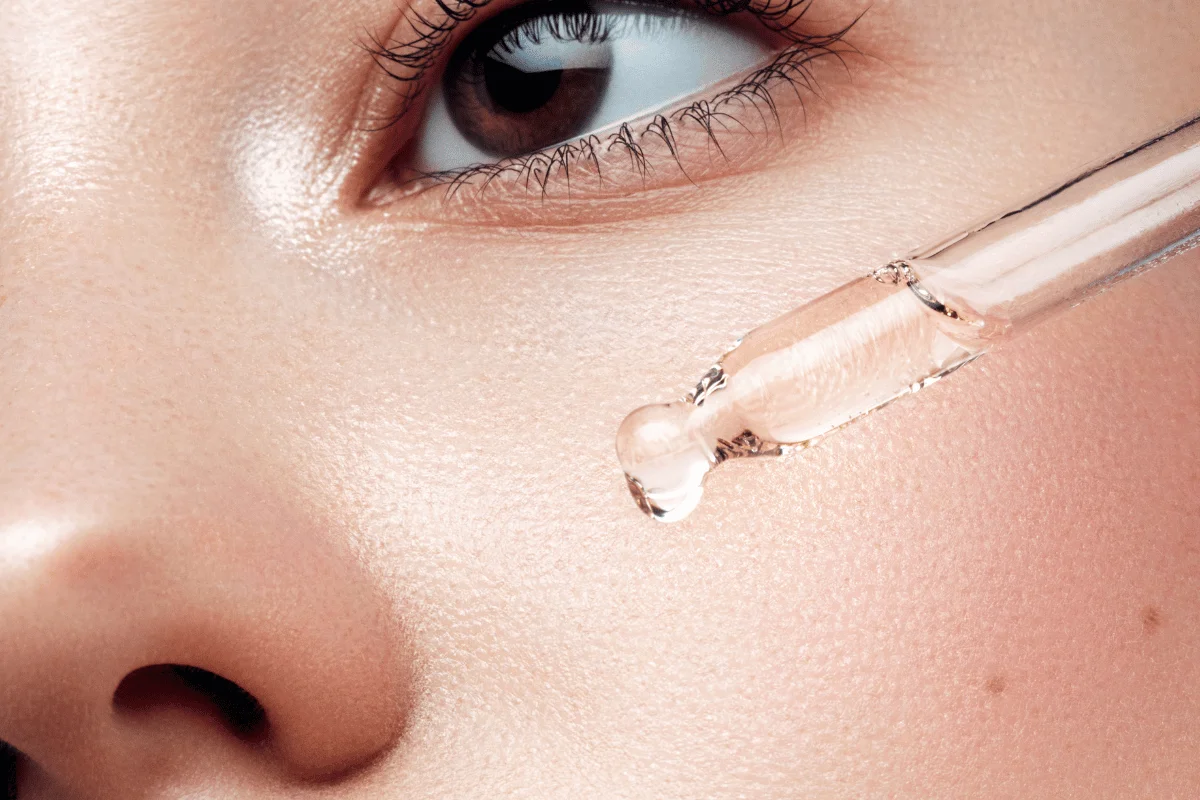 Close-up of a woman's face with a serum dropper applying skincare serum on her cheek.