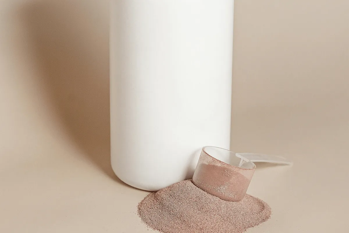 Large white container with a measuring scoop filled with light pink powder against a beige background.