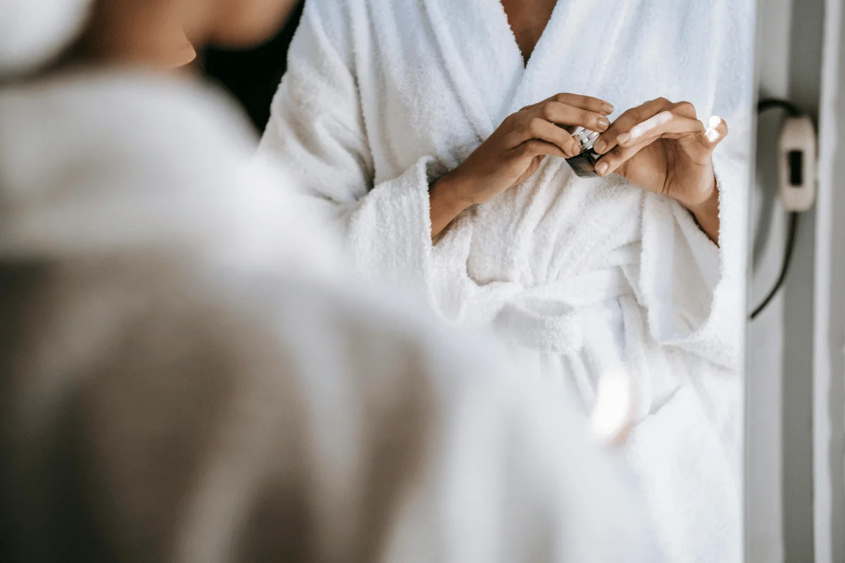 Close-up of a woman in a white bathrobe applying skincare serum in the bathroom.