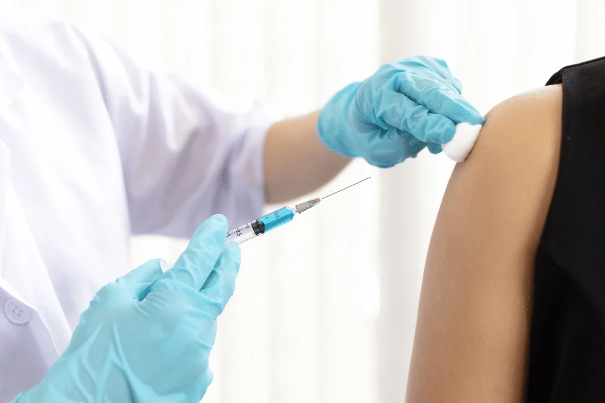 Healthcare worker administering injection to patient's arm with blue gloves.