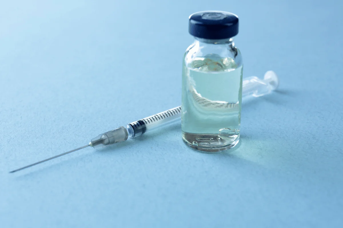 Close-up of a medical vial filled with liquid next to a syringe on a blue background.