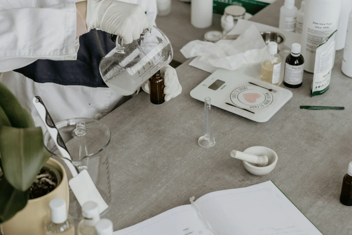 Lab technician pouring liquid into a brown glass bottle on a laboratory table filled with equipment.