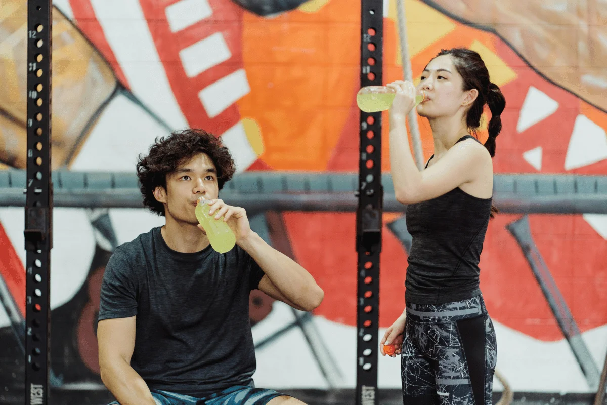 Two athletes enjoying a yellow sports drink during a gym break.