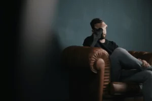 Man sitting on a leather couch with his hand on his face, appearing deep in thought.