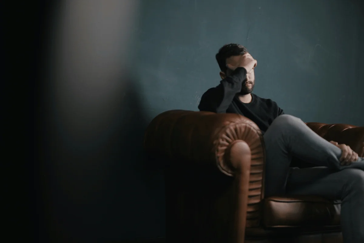 Man sitting on a leather couch with his hand on his face, appearing deep in thought.