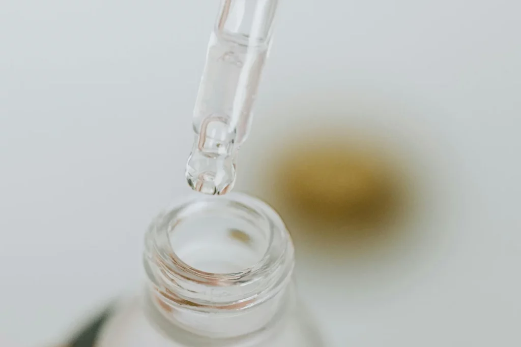 Skincare serum dropper releasing a clear liquid into a glass bottle.