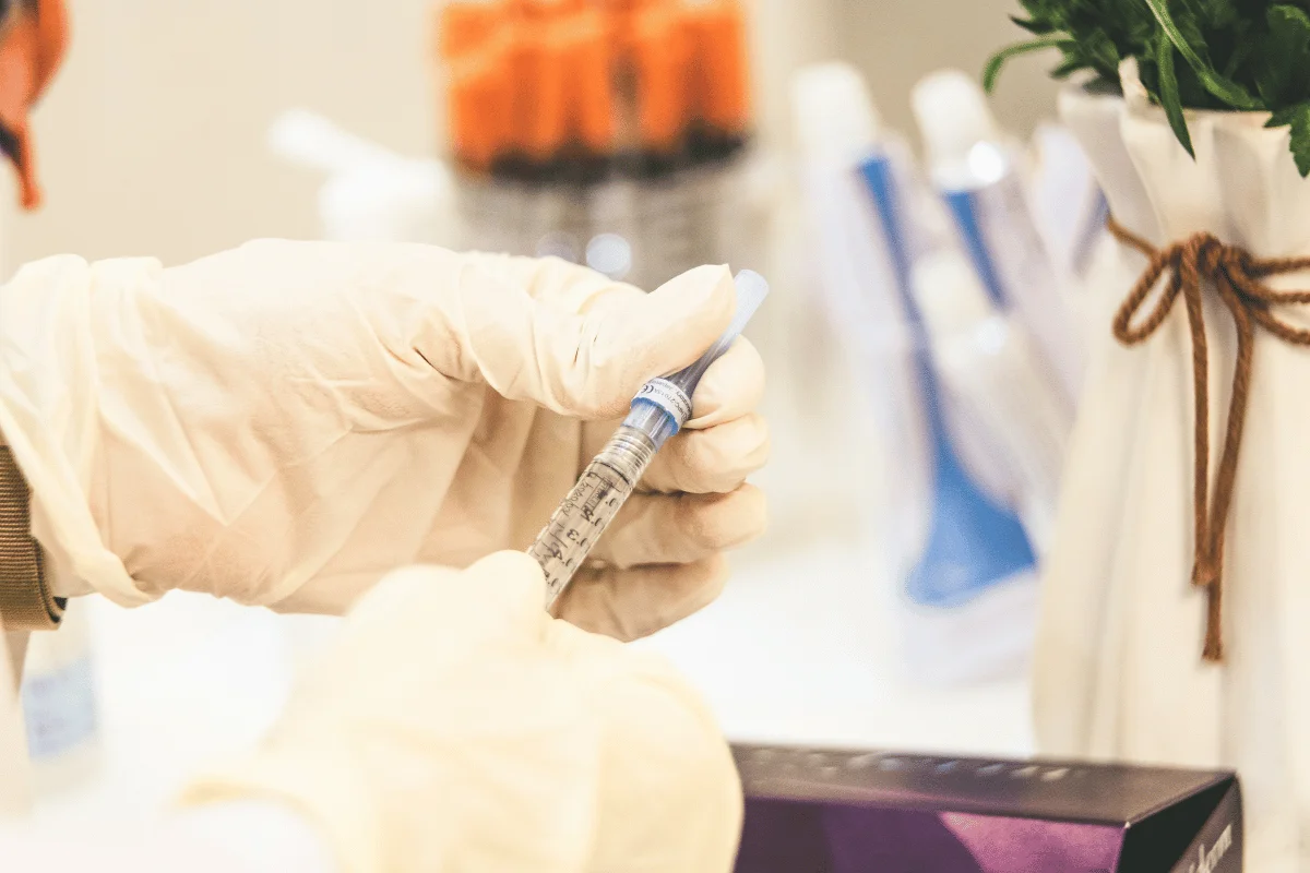 Gloved hands holding a syringe filled with liquid in a medical setting.