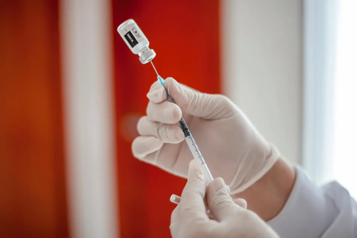 Close-up of gloved hands drawing vaccine into a syringe.