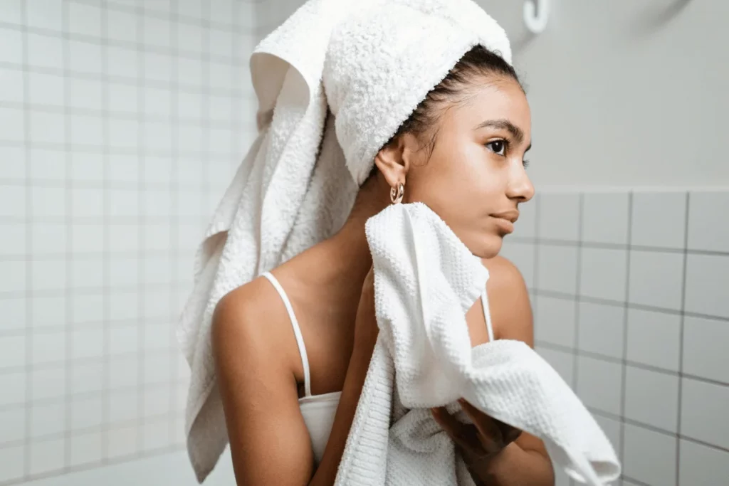 Woman drying her face with a towel in a tiled bathroom.