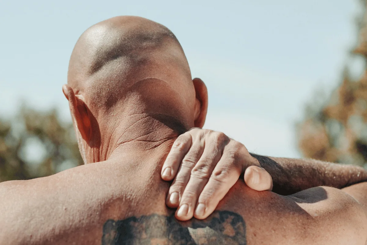 Person massaging their shoulder outdoors, showing discomfort.