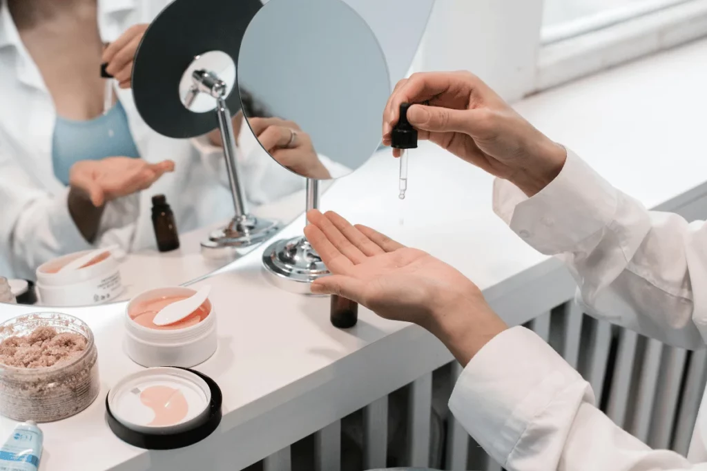 Woman applying skincare serum with a dropper, preparing for a beauty routine in front of a makeup mirror.