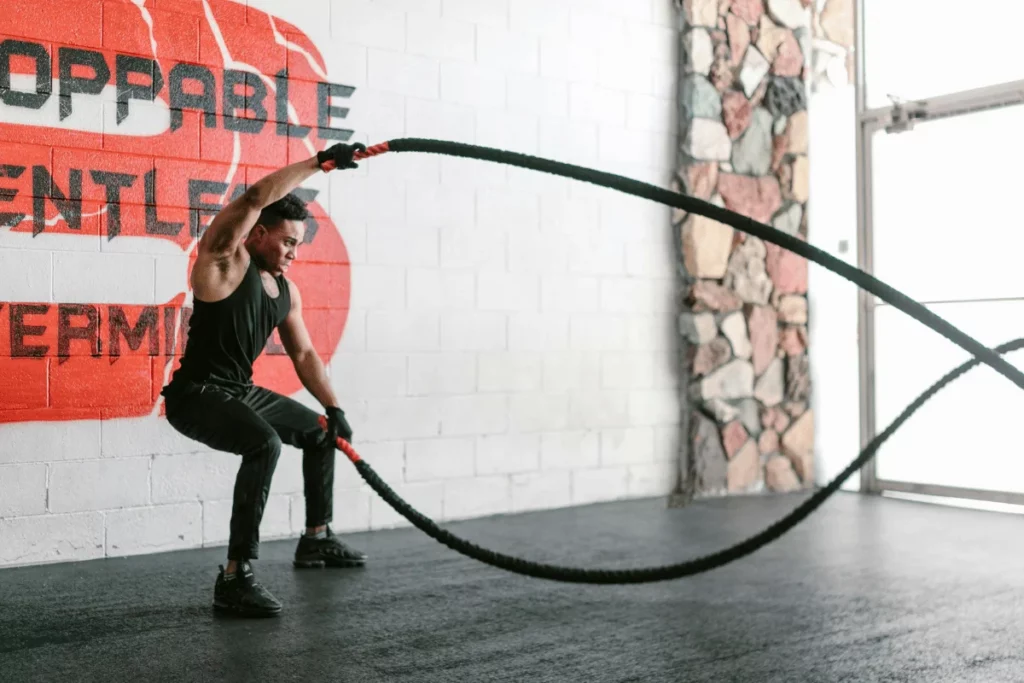 Athlete performing battle rope workout in a gym with motivational wall art.