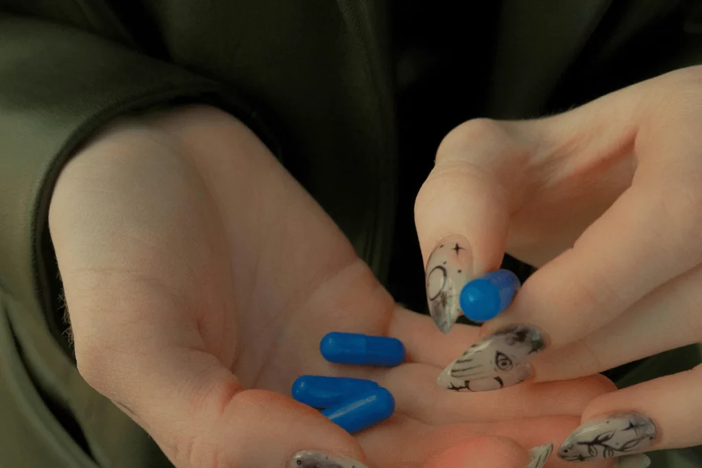 Close-up of a hand holding blue capsules with creative nail art.