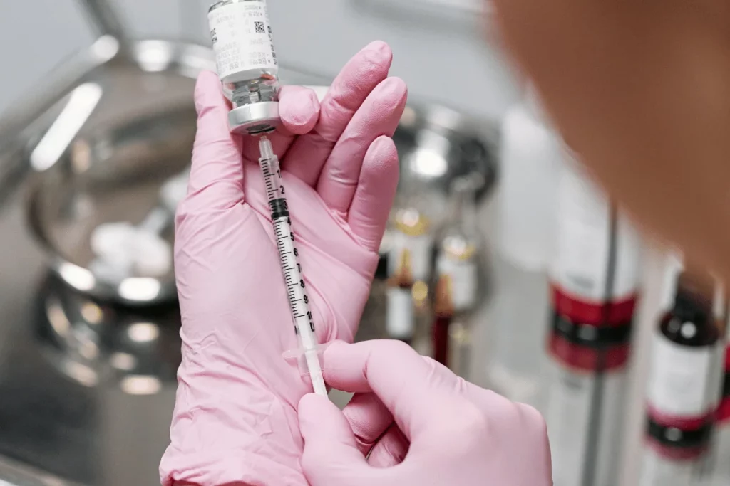 Healthcare worker in pink gloves drawing a vaccine dose from a vial using a syringe.