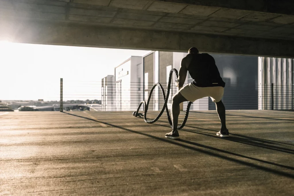 Man performing an intense battle rope workout outdoors in an urban setting at sunrise.