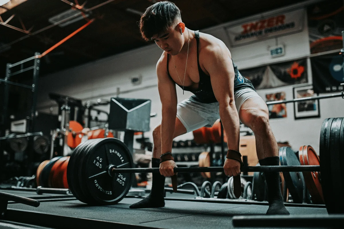 A muscular individual prepares to lift a heavy barbell in a well-equipped gym, demonstrating strength and focus.