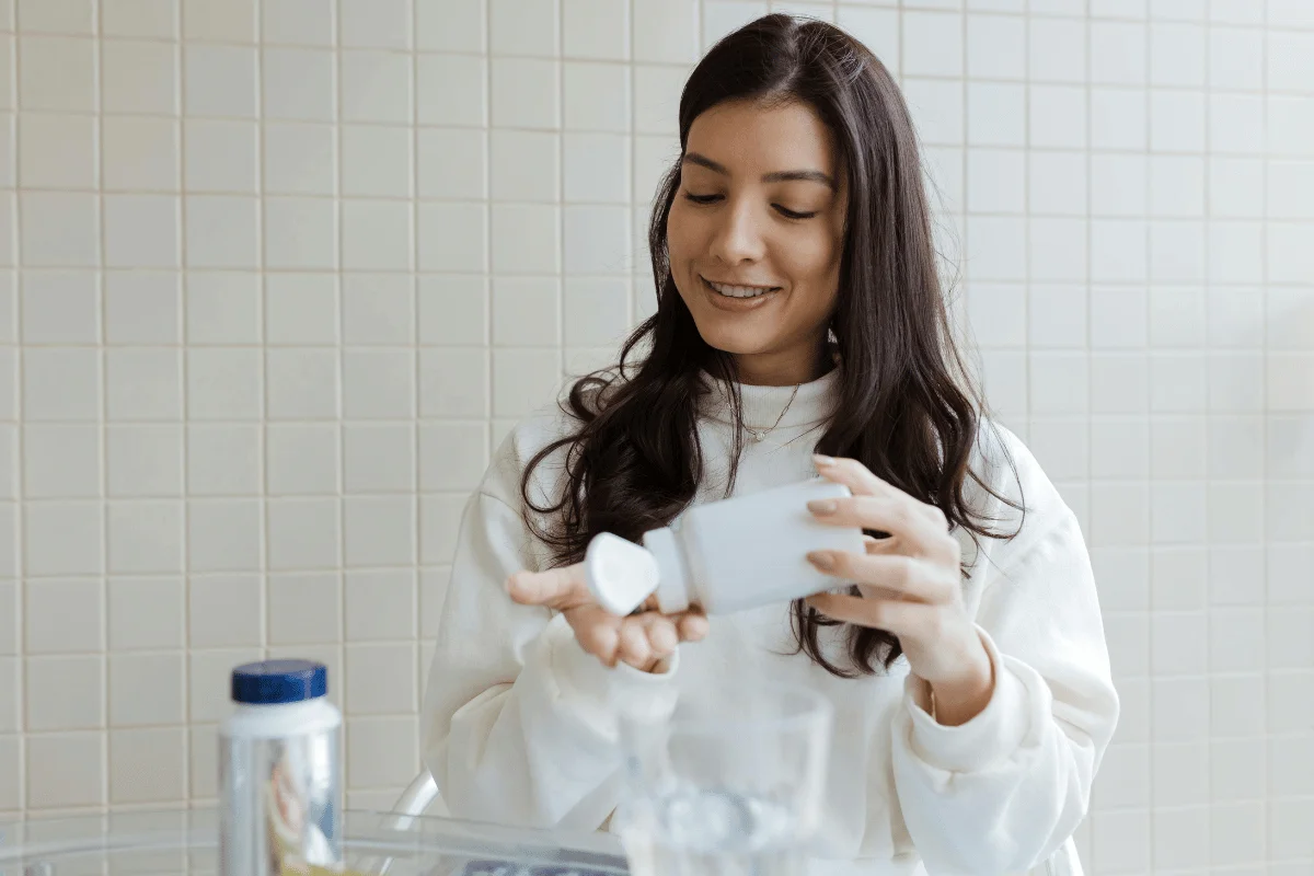 Smiling woman holding a bottle of supplements and pouring capsules into her hand.