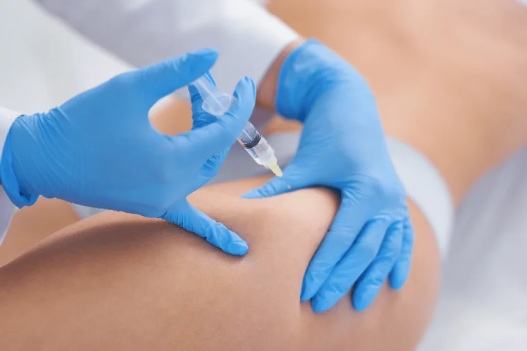 Medical professional in blue gloves injecting a syringe into a patient’s thigh.