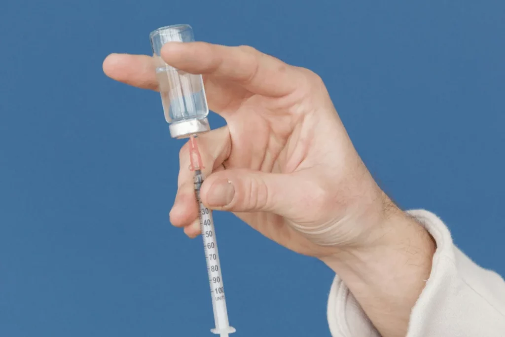 Close-up of a hand drawing liquid from a vial into a syringe against a blue background.