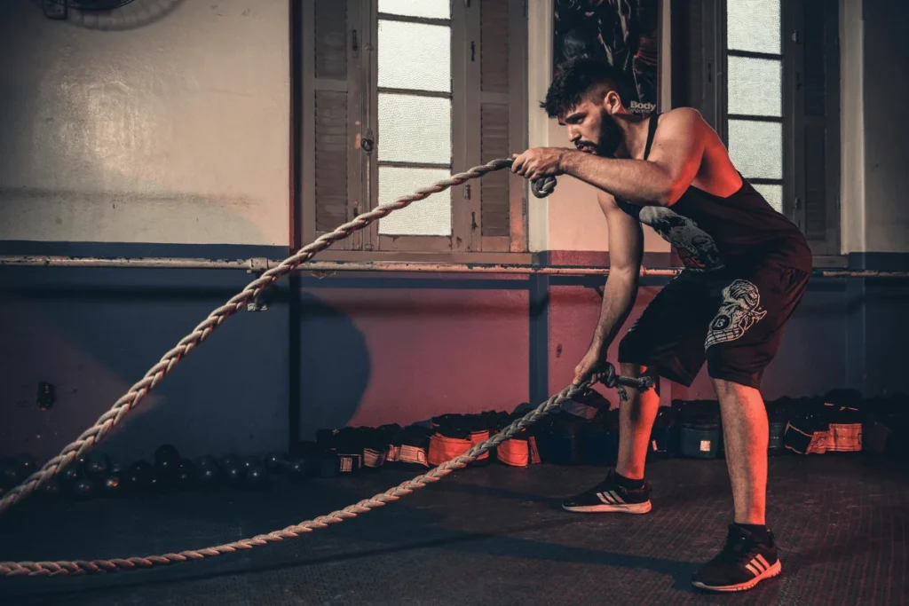 Man performing intense battle rope exercise in a dimly lit gym.