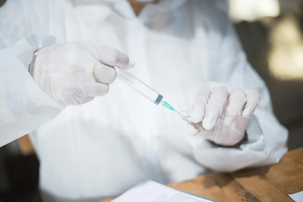 Healthcare worker in protective gear preparing a syringe with a vaccine or medication.