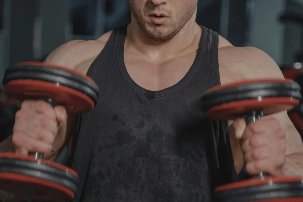 Close-up of a bodybuilder lifting dumbbells during an intense gym workout.