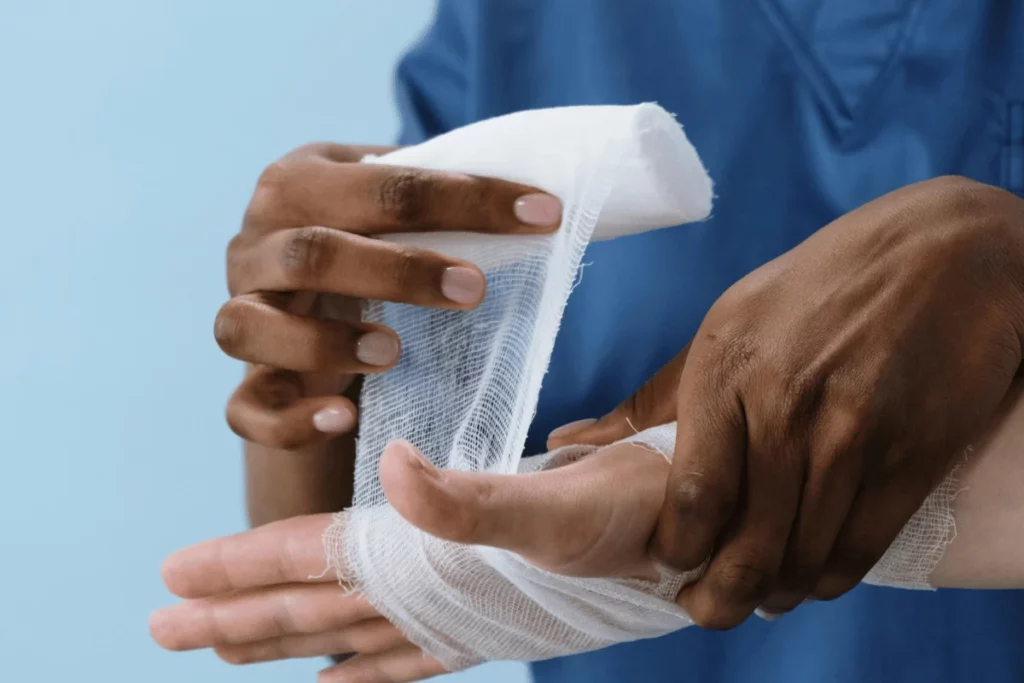 A healthcare professional wraps a bandage around a patient's hand, demonstrating proper first aid techniques.