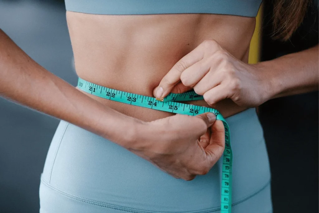 Close-up of a woman measuring her waist with a teal measuring tape.