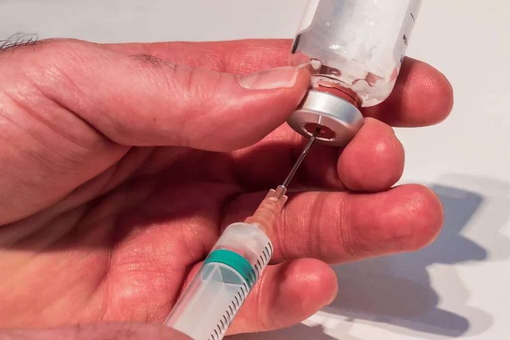 A close-up of a hand using a syringe to draw liquid from a vial, showcasing the needle entering the rubber stopper.