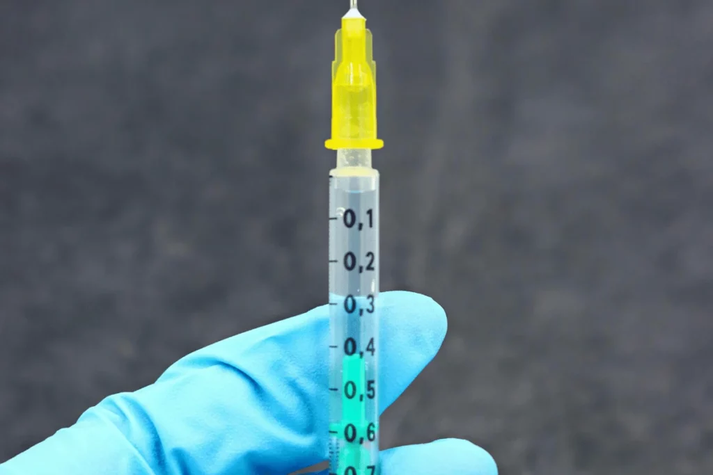 A gloved hand holding a syringe filled with a medical solution.