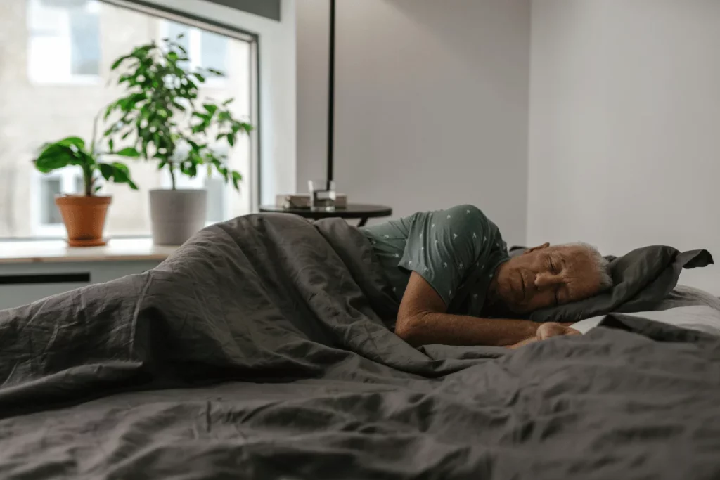 Elderly man sleeping peacefully in a cozy bed with dark bedding.