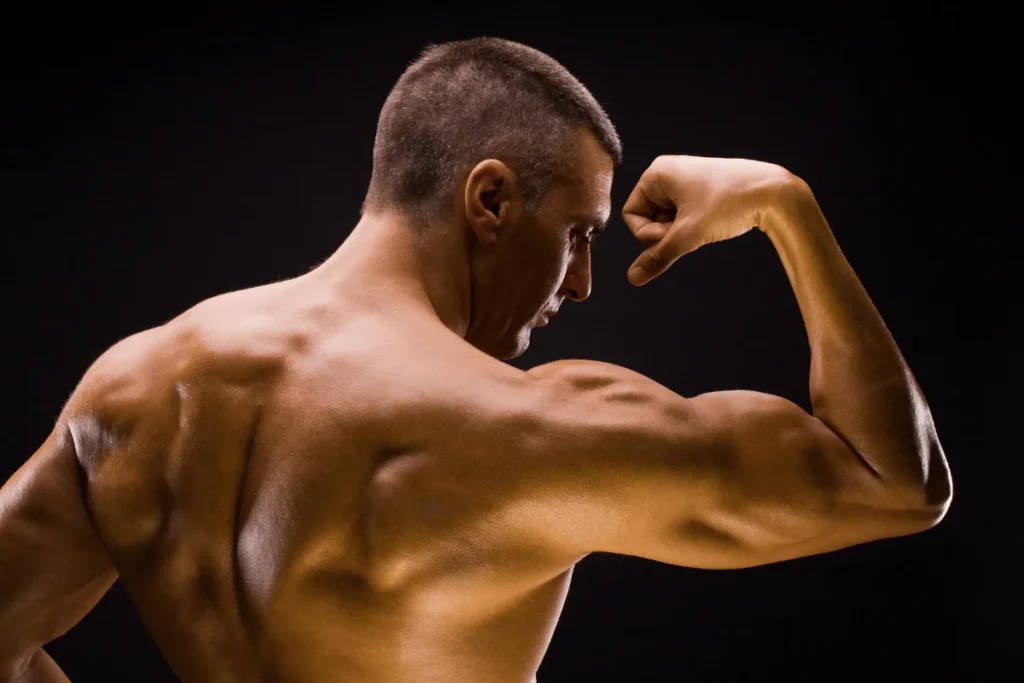 A muscular individual flexes their bicep, showcasing well-defined muscles against a dark, gradient background.