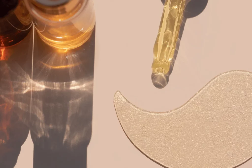 Golden skincare serum in a glass dropper with an under-eye patch.