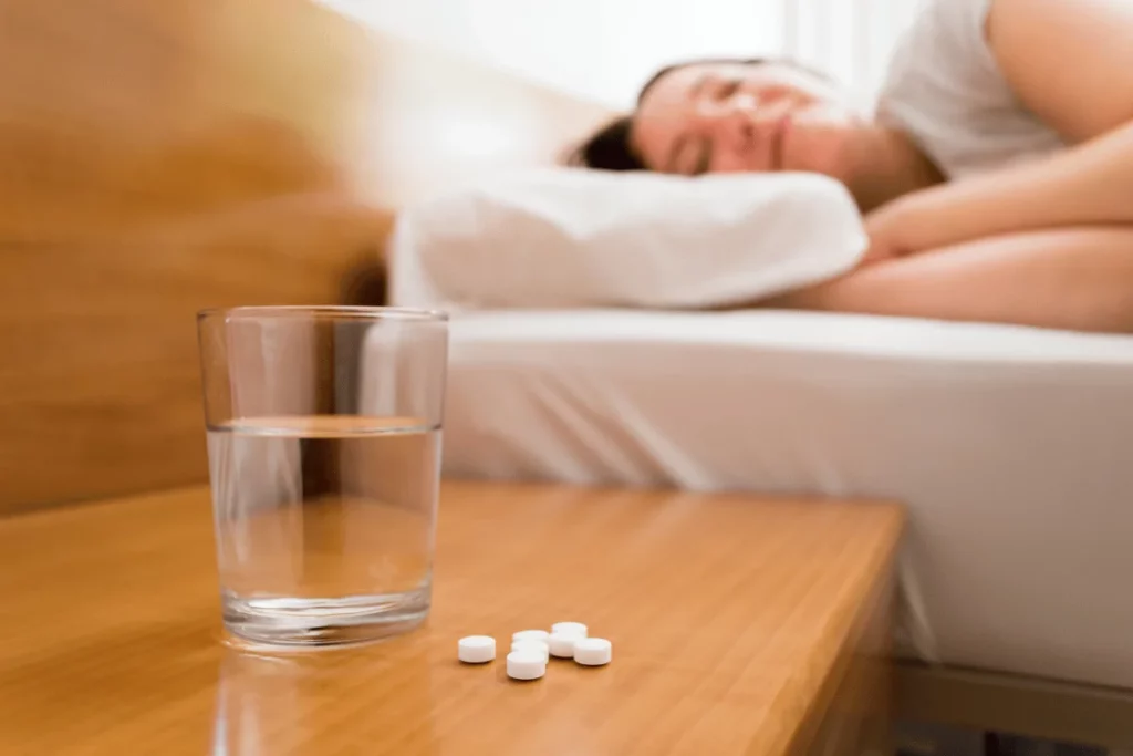 Nighttime routine: water and pills on a nightstand while a person sleeps peacefully.