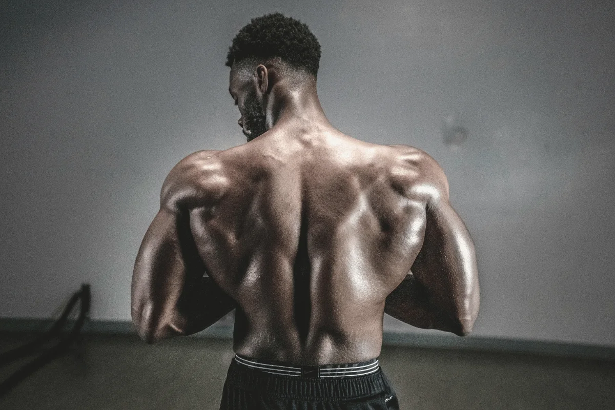 Close-up of a muscular back with defined shoulders and a smooth, shiny skin texture, showcasing strength and athleticism against a muted background.