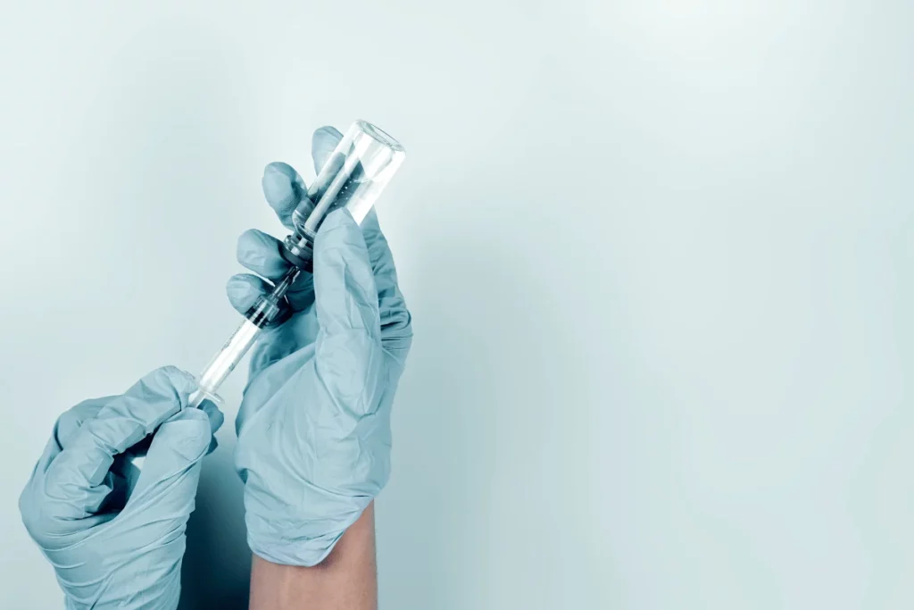 Gloved hands holding a syringe and vial for medication preparation.