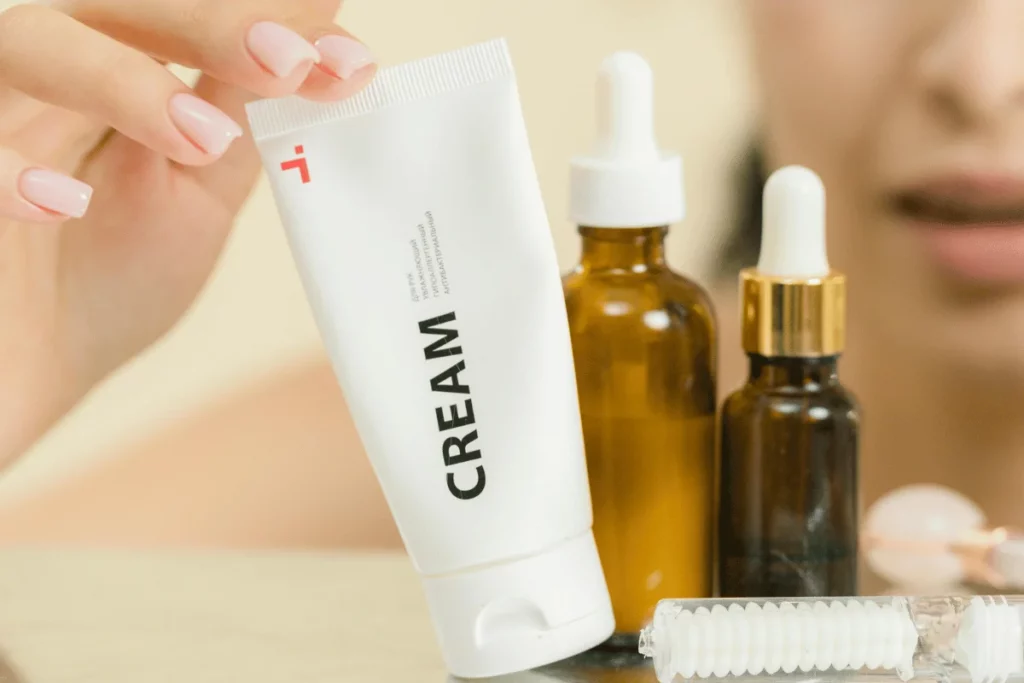 Close-up of a woman holding a skincare cream tube with serum bottles in the background.