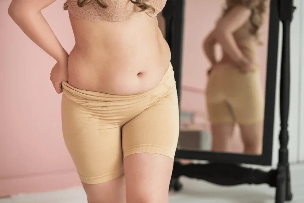 Close-up of a woman wearing a lace bra and beige compression shorts.