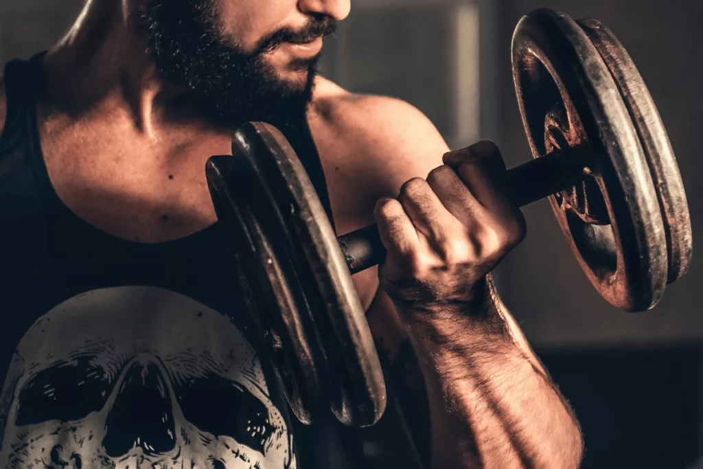 A close-up of a muscular arm lifting a rusty dumbbell, showcasing strength and focus in a dimly lit environment.