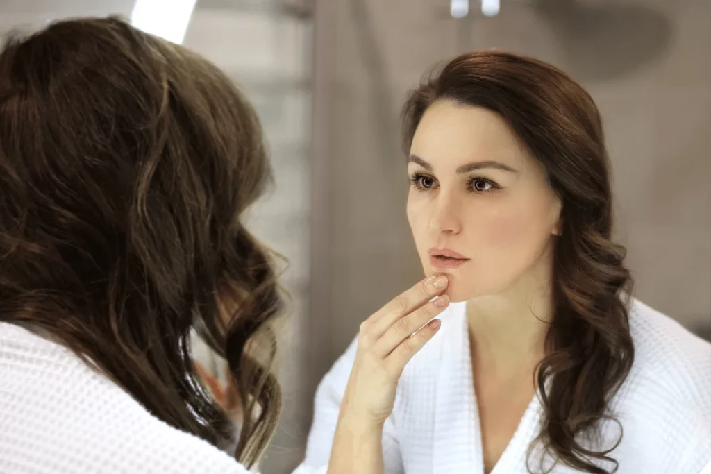 Brunette woman in a bathroom touching her face and checking her reflection.